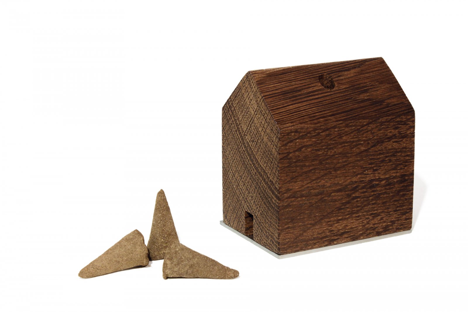 Ein kleiner räuchermännchen-rauchhaus-Halter aus Holz in Hausform, inspiriert von den Schwarzwaldhöfen und dem Designer Jan Hartmann, steht neben drei braunen Räucherkegeln auf weißem Hintergrund.