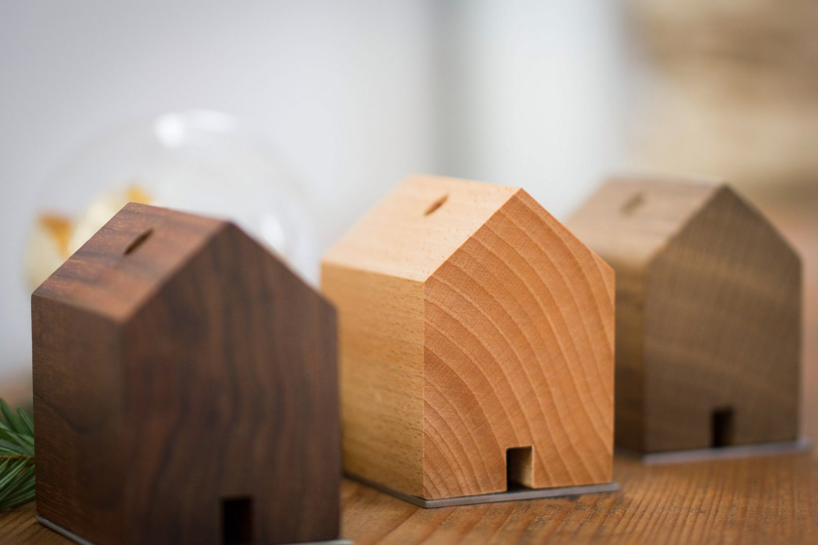 Drei holzhausförmige Objekte mit Schlitzöffnungen, inspiriert von Schwarzwaldhöfen und entworfen von Jan Hartmann, sind in einer Reihe auf einer Holzfläche angeordnet. Eine Anspielung auf das traditionelle RÄUCHERMÄNNCHEN RAUCHHAUS-Design.