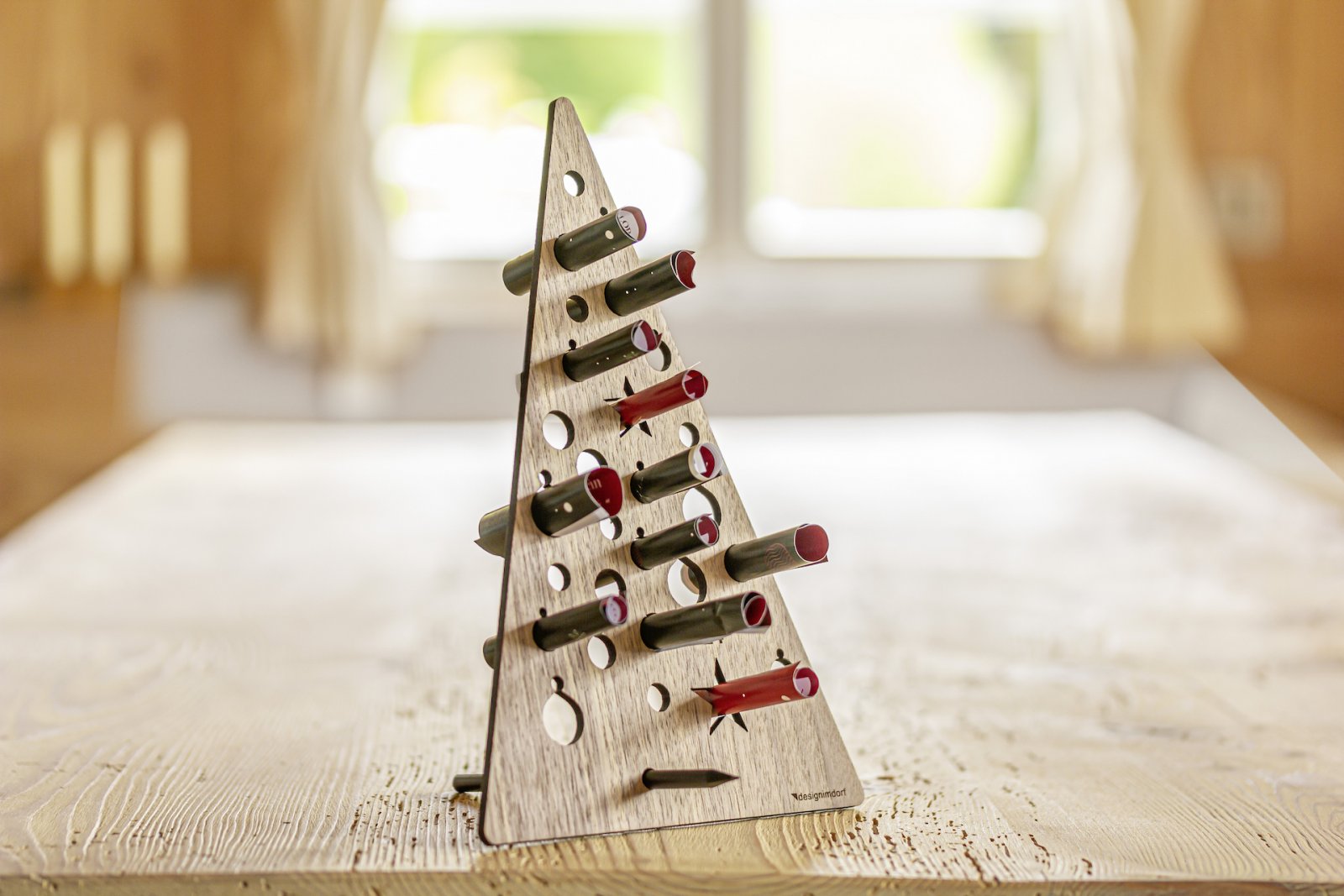 Dreieckiges Weinregal aus Holz mit mehreren Flaschen, platziert auf einem hellen Tisch vor einem Fenster – ideal als wiederverwendbarer Adventskalender für Weinliebhaber.