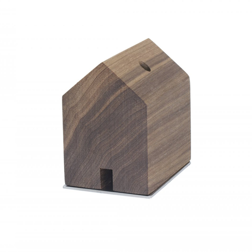 Ein kleines, hausförmiges Holzobjekt von Designer Jan Hartmann, inspiriert von Schwarzwaldhöfen, mit einem Schlitz oben und einer quadratischen Öffnung an der Vorderseite – perfekt als charmantes RÄUCHERMÄNNCHEN RAUCHHAUS.