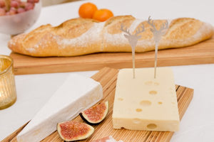 Käse, Feigen und Brot auf einem Holzbrett, mit dekorativen Hirschspießen im Käse – ein Arrangement inspiriert von Designerin Annegret Ewert-Wurster und gefertigt aus edlem Furnierschichtholz.