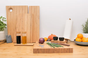 Holzschneidebretter aus der SAFARI Bretterserie, Kräuter, Gewürze und frische Produkte auf einer Küchentheke mit einer Küchenpapierrolle sorgen für Wärme und Funktionalität – und zeigen perfekt die Handwerkskunst von designimdorf aus Furnierschichtholz.