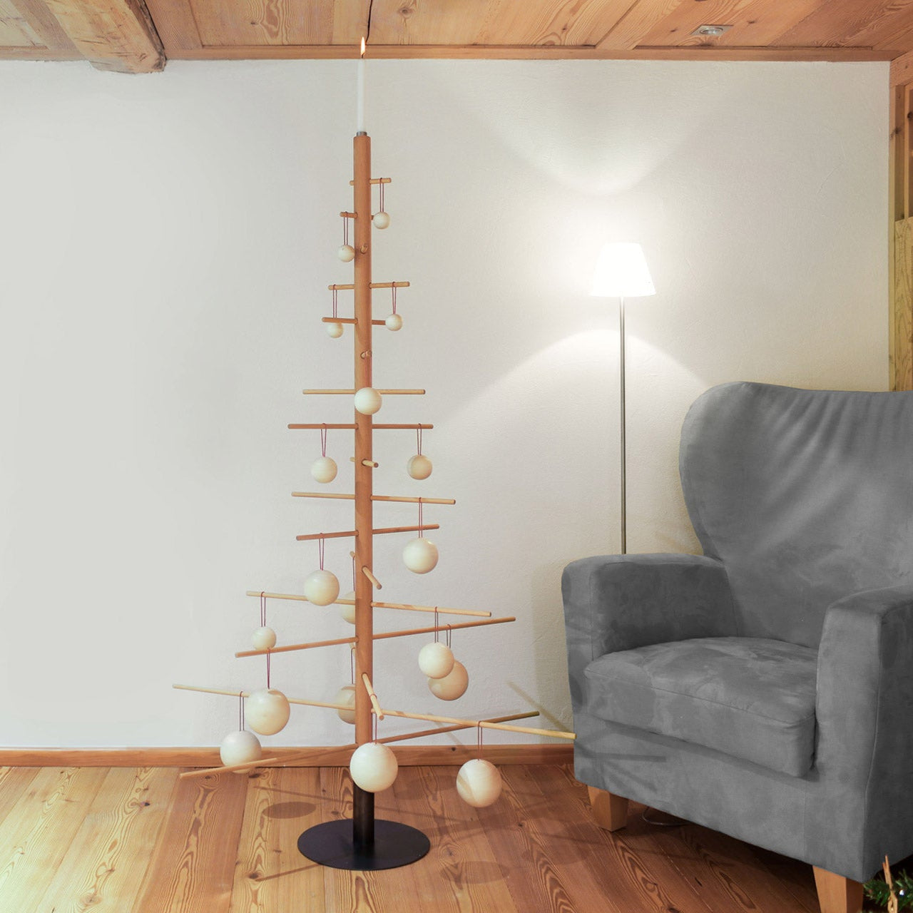 Minimalistischer abstrakter Baum aus Buchenholz mit einfachen Ornamenten in einem gemütlichen Wohnzimmer neben grauem Sessel und Lampe – die perfekte Wahl für nachhaltige Weihnachtsbäume.