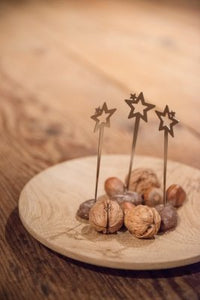 Nüsse auf einem Holzteller mit drei Sternenspießerchen auf einem Holztisch – ideal für unvergessliche Sternstunden bei Ihrer Weihnachtsparty.