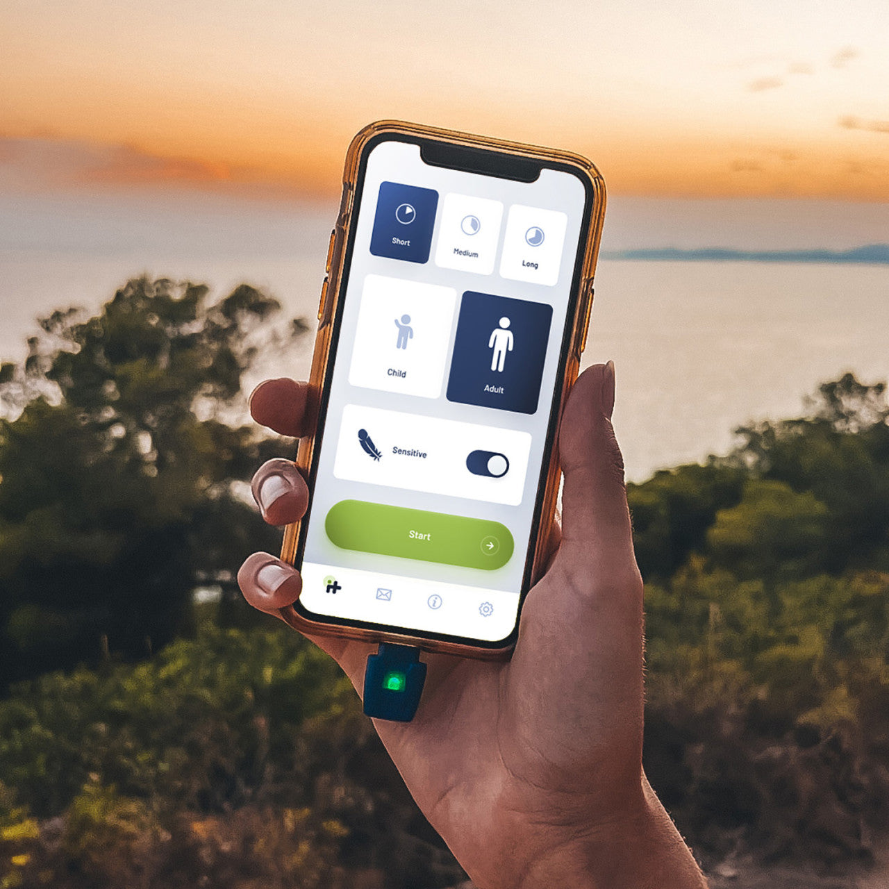 In der Hand hält man ein Smartphone mit geöffneter Heat it® Stichheiler-App zur Insektenstichbehandlung, im Freien in der Nähe von Wasser bei Sonnenuntergang.