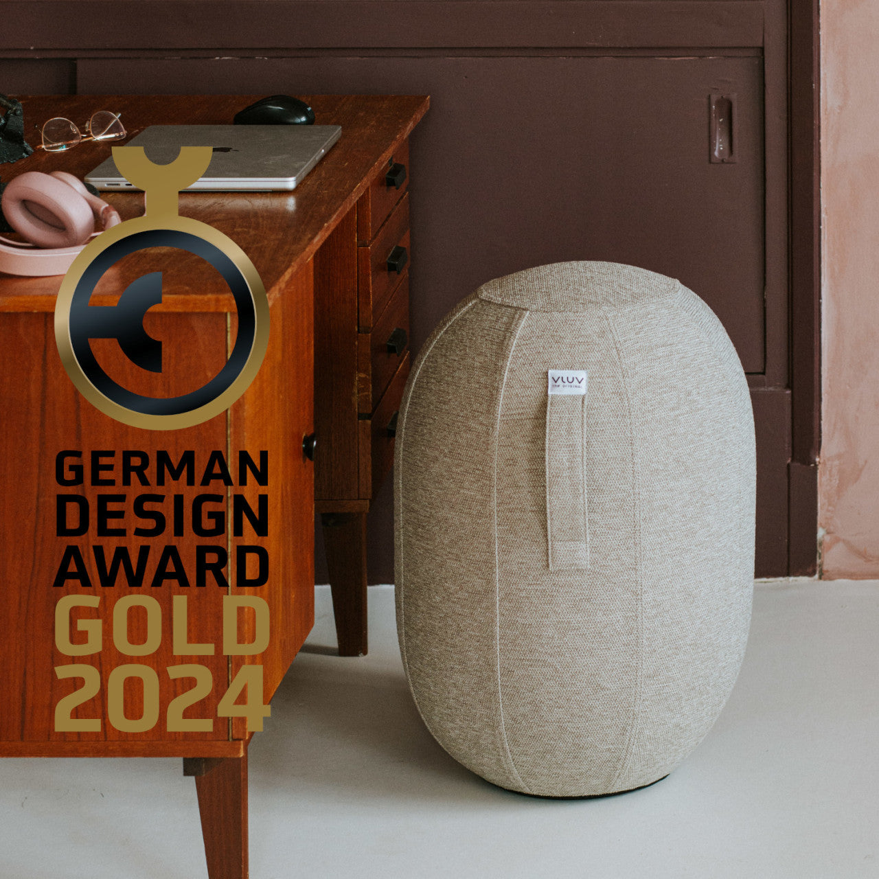 Ein luftgefüllter Sitzhocker neben einem Schreibtisch mit dem German Design Award Gold 2024-Logo und überlagertem Text bietet ergonomisches Sitzen für mehr Komfort.