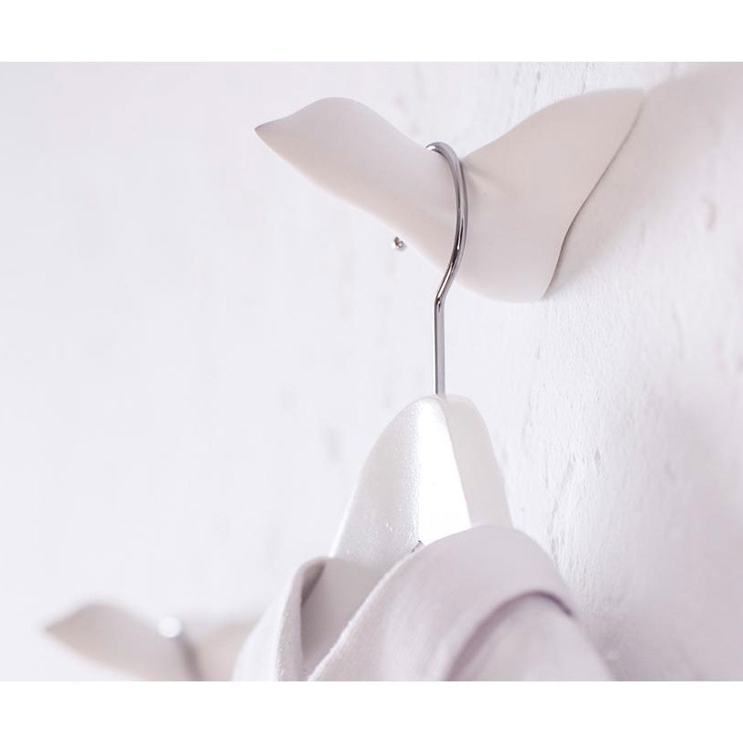 Weißer Mini Vogel als Wandhaken mit Kleiderbügel an weißer Wand