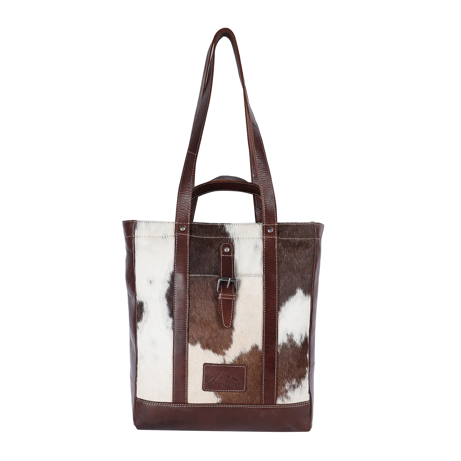Der Alpenleder Shopper HALLODRI ist eine braun-weiße Einkaufstasche aus Leder mit einem ausgeprägten Kuhfellmuster, einem Schnallendetail auf der Vorderseite, zwei stabilen Griffen und einem kleinen Logo-Patch am unteren Rand.