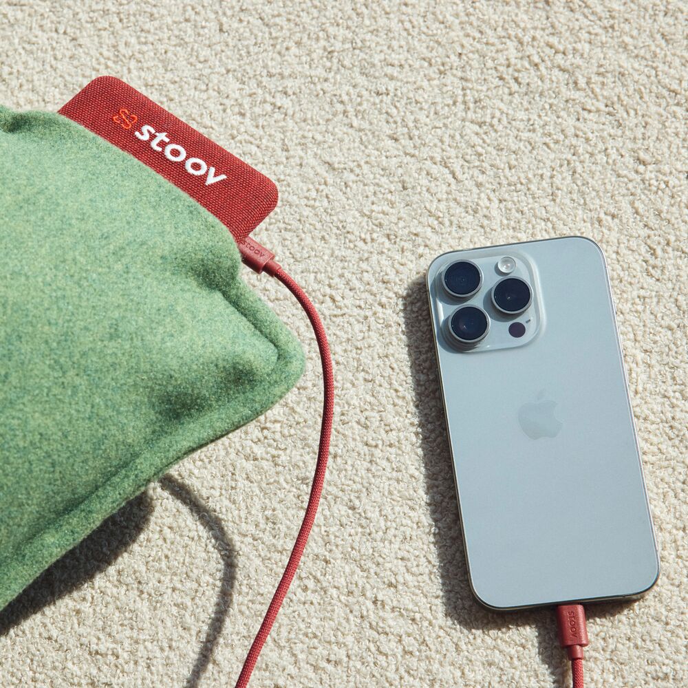Ein silbernes iPhone neben einem grauen Ploov Original Flex elektrisches Heizkissen.