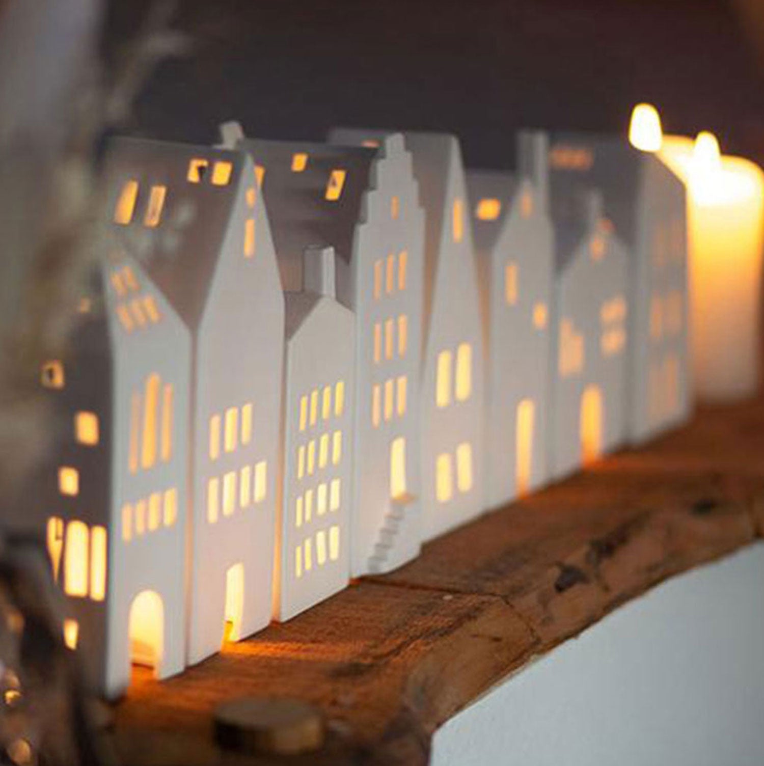 Eine Reihe von Lichthaus-„Turm“ steht auf einer Holzfläche, wird von innen durch warmes Kerzenlicht beleuchtet und schafft mit seinem charmanten rustikalen Design eine gemütliche und einladende Atmosphäre.