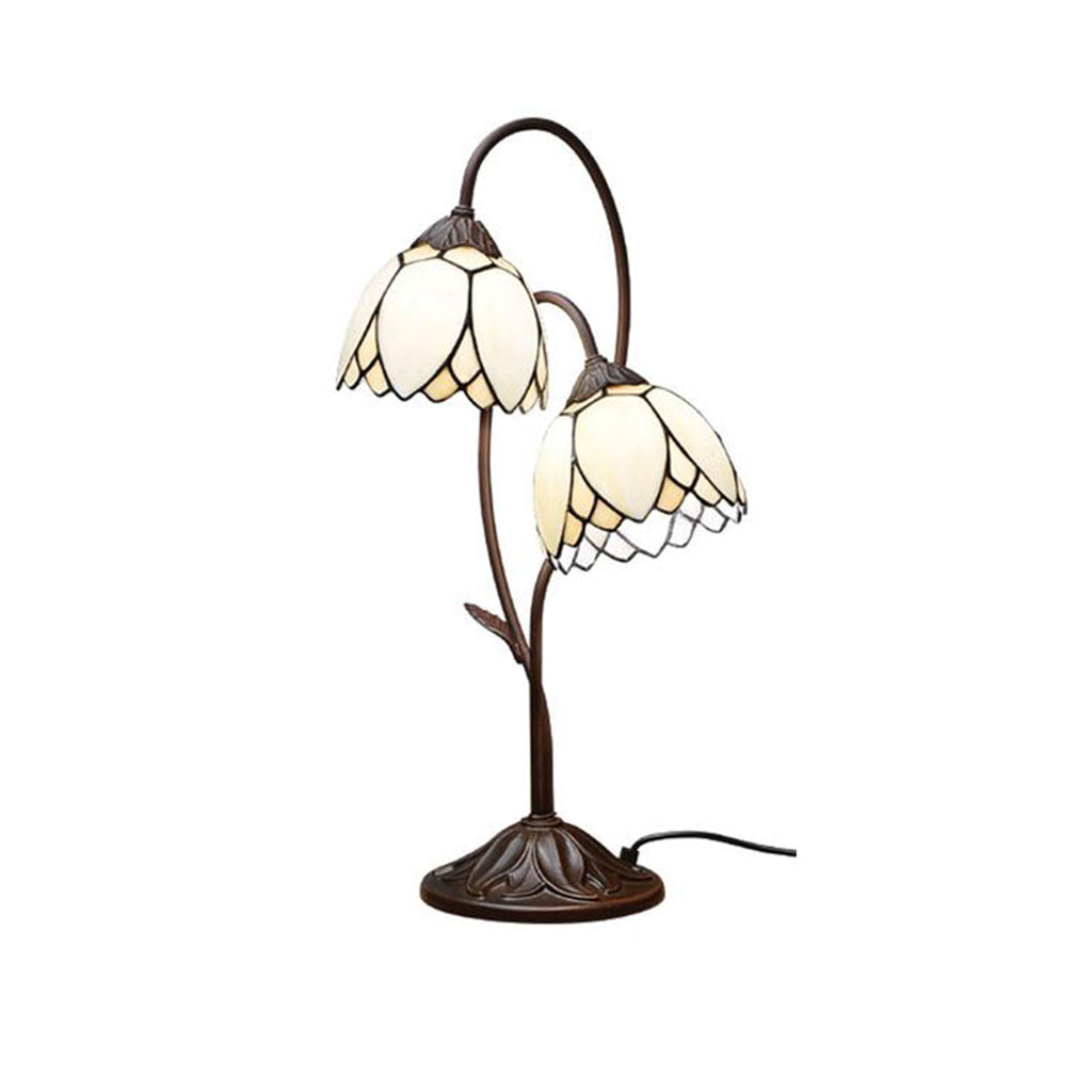 Die Tischlampe „Muguet“ besteht aus zwei blütenförmigen Lampenschirmen aus Buntglas auf geschwungenen Bronzestäben. Der verzierte Sockel mit Blattmotiven harmoniert mit den Schirmen, die an weiße Blütenblätter mit dunklem Rand erinnern.