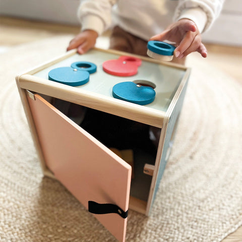 Ein Kind erkundet eine Sinnes- und Fühlbox, indem es farbige Formen und Linsen in passende Löcher steckt und so das Spielen in ein lustiges Sinnes- und Fühlbox-Erlebnis verwandelt.