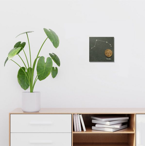 Eine Topfpflanze auf einem weißen Schrank neben einem Wandbild mit einem Sternbild und einem goldenen Löwensymbol, akzentuiert mit schillernden Swarovski-Elementen für einen Hauch von Eleganz.