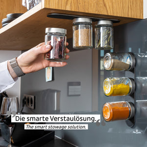 Eine Hand greift nach einem Gewürzglas aus einem magnetischen Gewürzregal und präsentiert Magnetkraft und eine innovative Verstaulösung für Gläser unter dem Küchenregal.
