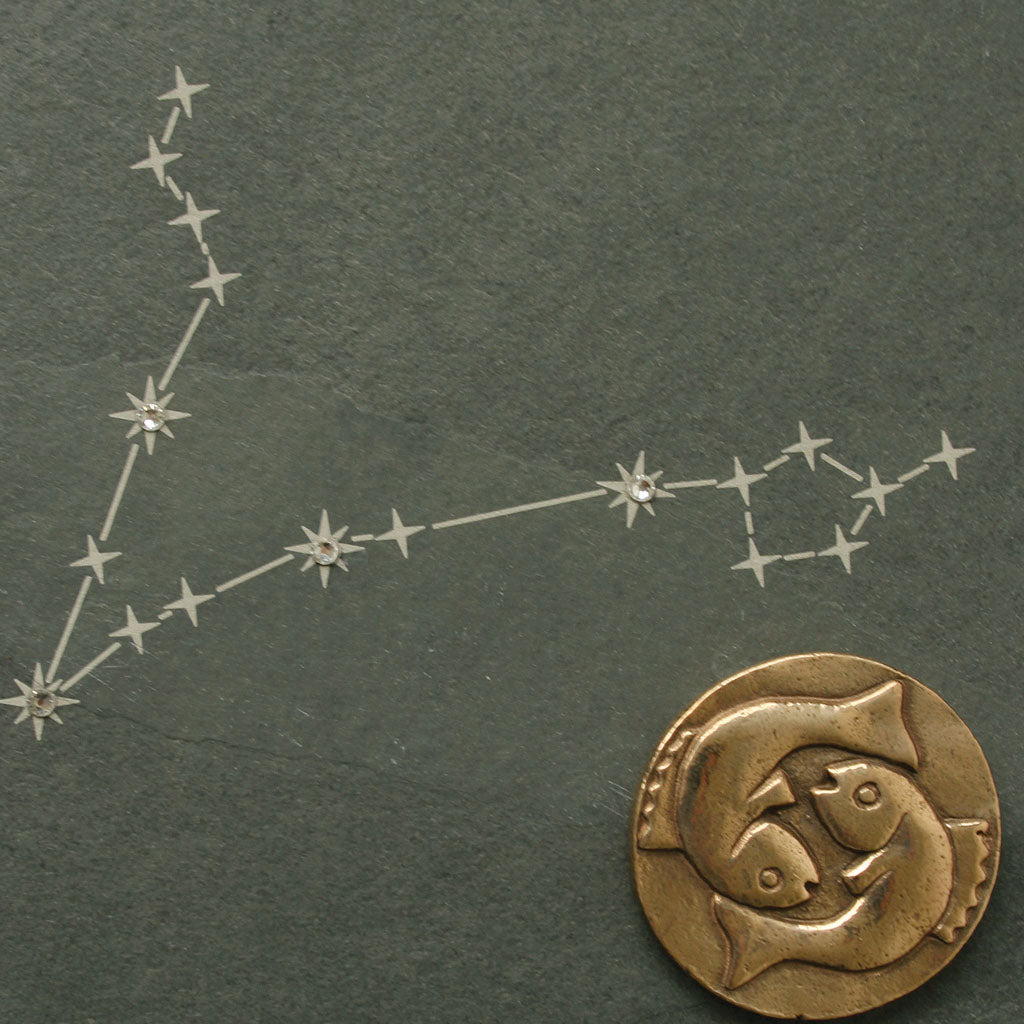 Sternbild Fische auf dunkler Naturschiefer-Oberfläche gezeichnet, darunter eine Bronzemünze mit zwei Fischen.