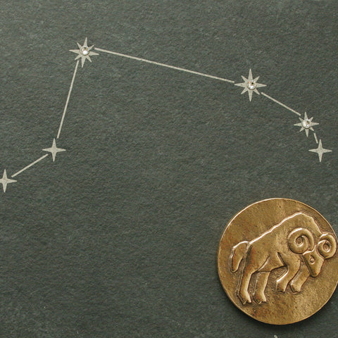 Goldenes Widder-Emblem und Sternbildzeichnung auf dunklem Hintergrund. Dieses elegante Design hebt das Sternzeichen auf einem an Naturschiefer erinnernden Hintergrund hervor, akzentuiert mit funkelnden Swarovski-Elementen.