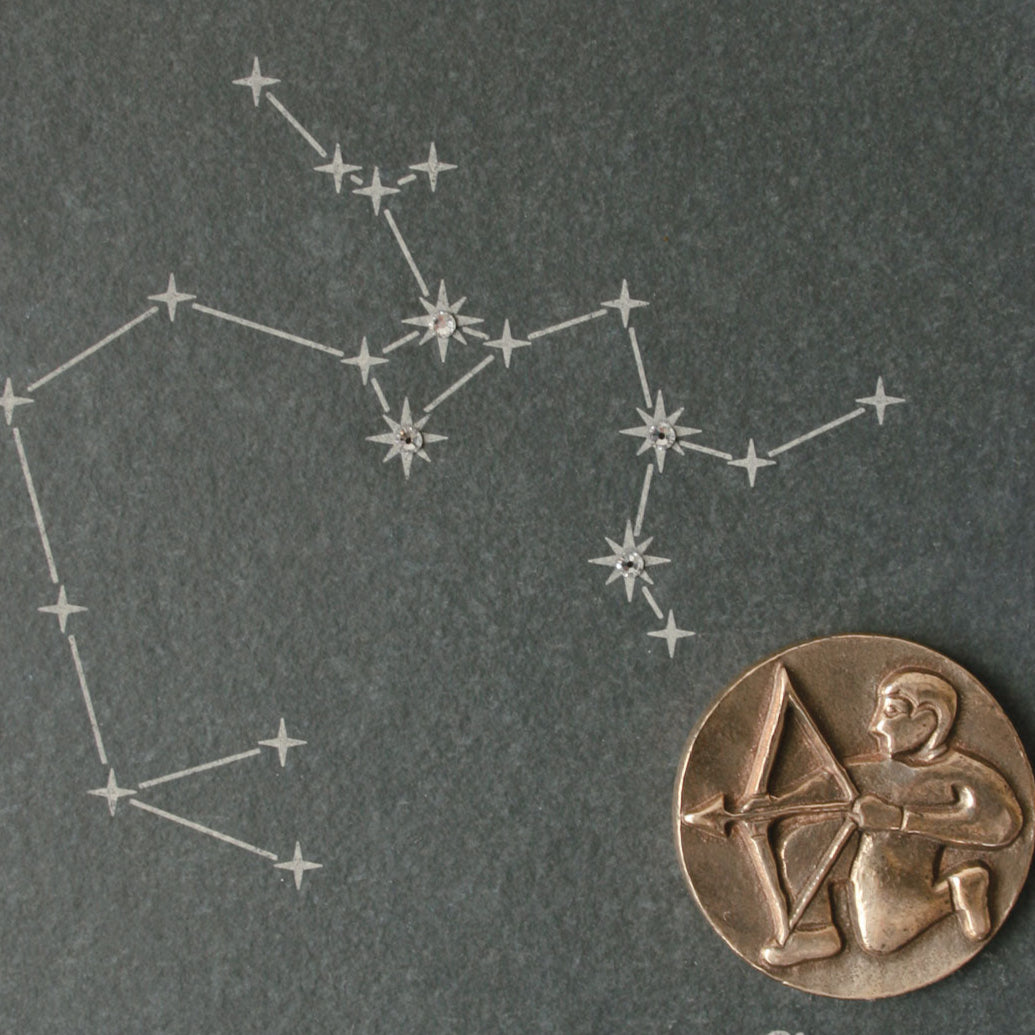 Zeichnung des Sternbildes Schütze mit einer bronzenen Schütze-Bogenschütze-Münze, akzentuiert durch funkelnde Swarovski-Elemente .