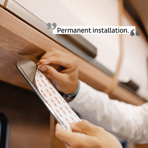 Hände bringen einen Klebestreifen mit der Aufschrift „Dauerhafte Installation“ auf einer Oberfläche unter einem Regal an. Magnetkraft hält Gläser sicher an ihrem Platz – eine innovative Verstaulösung.