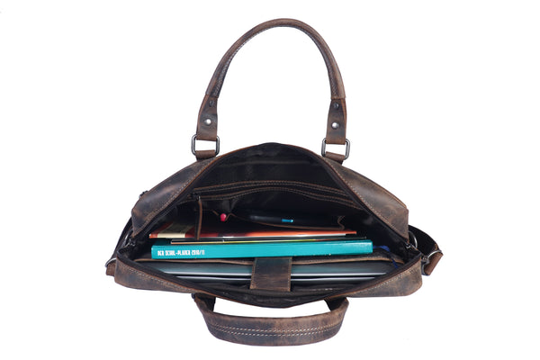 Eine braune Aktentasche LUDWIG aus Büffelleder, gefertigt mit pflanzlicher Gerbung, öffnet sich und gibt den Blick auf Bücher, ein Notizbuch, Stifte und einen Laptop frei.