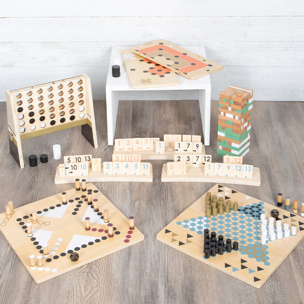Eine Vielzahl von Brettspielen und Spielsteinen aus Holz, darunter auch ein Rommé-Spiel mit Holzplättchen, sind ordentlich auf einem Holzboden angeordnet.