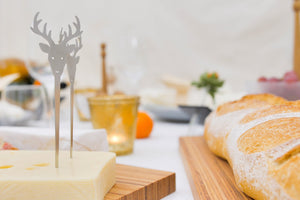 Ein Käseblock mit einem Edelstahl-Hirschspieß neben Brotlaiben auf einem Holzbrett – perfekt für Ihre nächste Party.