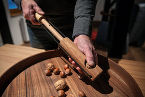 Nahaufnahme von Händen, die mit einem von Dietmar Mechsner gefertigten Nussknacker aus Holz eine Walnuss über einem Tablett mit verschiedenen Nüssen knacken.